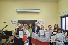 Grupa uczniów i nauczycieli prezentuje certyfikaty Erasmus+ oraz polską flagę w sali szkolnej.
