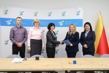 W sali konferencyjnej stoją osoby uczestniczące w podpisaniu umowy wymienione w artykule, pani burmistrz podaje dłoń pani reprezentującej wykonawcę robót
