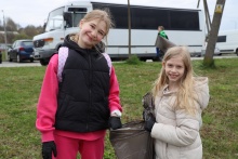 Dwie dziewczynki sprzątają teren i trzymają worek na śmieci.