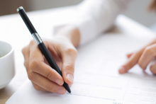 dłoń trzymajaca długopis wypełniająca dokument który leży na stole