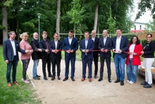 Grupa osób podczas uroczystego przecięcia czerwonej wstęgi w parku.