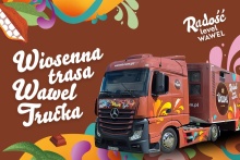 Kolorowa grafika promująca Wiosenną Trasę Wawel Trucka. Na ilustracji czerwony samochód ciężarowy marki Wawel na brązowym tle z dekoracyjnymi, wiosennymi motywami.