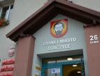 Wejście do budynku Urzędu Gminy i Miasta Dobczyce z widocznym herbem Dobczyc oraz napisem „Gmina i Miasto Dobczyce”. Na elewacji widoczny numer adresowy: Rynek 26.
