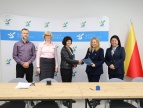 W sali konferencyjnej stoją osoby uczestniczące w podpisaniu umowy wymienione w artykule, pani burmistrz podaje dłoń pani reprezentującej wykonawcę robót