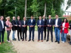 Grupa osób podczas uroczystego przecięcia czerwonej wstęgi w parku.