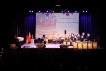 widok na scenę z tyłu auli w tle sceny widać baner z grafiką tortu i napisem urodziny partnerstwa, przemawia burmistrz Versmold
