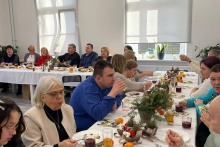 uczestnicy spotkania wigilijnego siedzą przy świątecznie ubranym stole na którym jest ciasto i potrawy 
