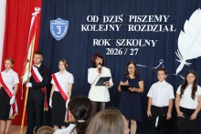 Uczniowie i nauczyciele podczas uroczystości rozpoczęcia roku szkolnego 2026/2027. W tle napis „Od dziś piszemy kolejny rozdział” i szkolny sztandar.