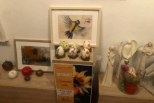 na ścianie wiszą obrazy a na półce stoją formy przestrzenne wykonane z kolorowych pasemek wełny