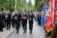 Strażacy niosący czerwono-białą flagę Polski. Tuż obok widnieją sztandary