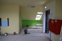 Sala przedszkolna w trakcie remontu. Ściany mają kolor żółty i zielony a na ścianie z prawej strony wisi czerwona skrzynka