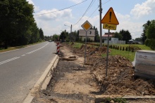 Na zdjęciu widnieje rozkopana ziemia podczas budowy chodnika. Z boku chodnika stoi pomarańczowy znak z wykrzyknikiem w środku