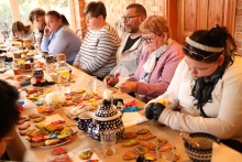 wzdłuż stołu siedzą uczestnicy warsztatów i dekorują pierniki na stole widać udekorowane pierniki