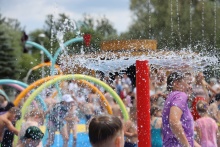 na pierwszym planie sikająca wodą konstrukcja, w tle rozmazane bawiąze się na placu zabaw dzieci