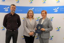 trzy osoby na tle ścianki z logami gminy: kierownik Konrad Skiba, wiceburmistrz Edyta Podmokły oraz wykonawca Iwona Gryglak