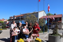 dzieci z niepełnosprawnością wraz z opiekunami ustawieni na tle flag narodowych trzymają w rękach kosze z piernikami w barwach narodowych, które będą wręczać uczestnikom obchodów 