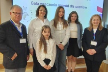 Na zdjęciu uczestnicy Forum Wymiany Doświadczeń i Gali Wręczenia Nagród projektu „Małopolski Program Wspierania Uczniów”. Przed ekranem z nazwą wydarzenia stoją uczennice, nauczycielki oraz przedstawiciel samorządu i organizatorów. Uroczystość odbyła się w Krakowie i była podsumowaniem realizacji programu wspierającego rozwój talentów uczniów.