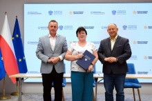760 tys. zł dla Gminy Dobczyce na budowę magazynu obrony cywilnej od lewej stoi burmistrz Tomasz Suś, obok niego Główna Księgowa renata Banowska, która w trzyma w rękach granatową teczkę typu ofertówka, po prawejs tronie stoi Wojewoda Krzysztof Jan Klęczar, w tle widać flagi Polski i Unii Europejskiej oraz duzy baner z logami Oprogramu Ochrona ludności i obrona cywilna