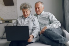 dwie starsze osoby siedzące na kanapie z laptopem w rękach 