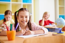 dziewczynka z uśmiechem siedząca w szkolnej ławce