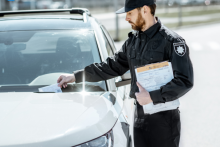 policjant wkładający manadat za szybę białego samochodu