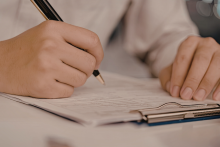 dłoń trzymajaca długopis wypełniająca dokument wpiety w podkładkę biurową