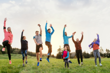 osoby w różnym wielku podskakują na trawie z rękami wyciągniętymi ku górze