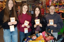 Cztery dziewczyny w sklepie stoją przy koszu z żywnością i plakacie zbiórki wielkanocnej.