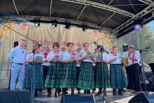 Grupa kobiet w tradycyjnych strojach ludowych występuje na scenie podczas wydarzenia plenerowego.