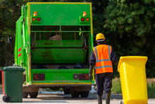 pracownik ciągnie kubeł na śmieci przed nim stoi śmieciarka