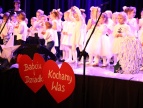 przedszkolaki ubrane na biało występują na scenie, do przodu sceny przytwierdzone są dwa wielkie czerwone serca na których widnieje napis babciu i dziadku kochamy was 