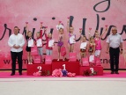 na podium stoją laureatki turnieju trzymają uniesione w górę puchary, z lewej strony laureatek stoi burmistrz Tomasz Suś a z prawej dyrektor MGOKiS Andrzej Topa  