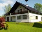 biały dom z brązowym dachem, przed nim zielony trawnik 