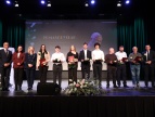 Na scenie podczas uroczystej gali stoją w rzędzie laureaci nagrody burmistrza w dziedzinie sportu, każdy z nich trzyma statuetkę i różę,  wraz z przedstawicielami samorządu 