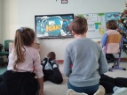 dzieci siedzą w sali lekcyjnej, na ekranie telewizora wyświetlany jest materiał filmowy o projekcie byćja Ignacy