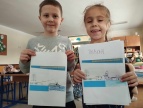 dwoje dzieci stoi obok siebie i prezentują swoje prace plastyczne: schemat elektrowni wodnej