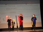grono dzieci w czarno-czerwonych strojach podczas występu na scenie 