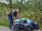 Zdjęcie przedstawia pracownika Urzędu, który składa w jednym miejscu część zebranych worków śmieci podczas akcji sprzątania terenów leśnych Kornatki.