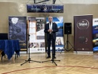 mężczyzna w czarnym garniturze mówiący przez mikrofon 