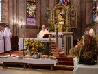 ksiądz odprawiający mszę świętą z boku służba liturgiczna, przed ołtarzem chleby i kołacze ofiarowane przez rolników po bokach ułożone sa wieńce dożynkowe 