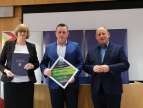 Stoją od lewej: skarbnik, burmistrz oraz wojewoda. Burmistrz trzyma ramkę z informacją o przyznanej promesie