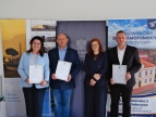 Dodatkowe środki dla Środowiskowego Domu Samopomocy w Dobczycach Na zdjęciu cztery osoby stoją podczas uroczystego spotkania - od lewej: przewodnciząca rady miejskiej, wojewoda, kierownik ŚDS oraz burmistrz. Dwie osoby trzymają dyplomy z podziękowaniami. W tle widoczne są roll-upy promocyjne oraz baner Środowiskowego Domu Samopomocy w Dobczycach. Uczestnicy są ubrani w stroje formalne i pozują do wspólnego zdjęcia.