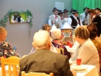 Wigilijne spotkanie mieszkańców gminy Dobczyce Kilka osób siedzących przy stoliku i patrzących w kierunku grupy kolędniczej- Werdebusy Dobczyckie