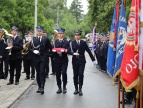 Strażacy niosący czerwono-białą flagę Polski. Tuż obok widnieją sztandary