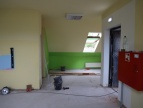 Sala przedszkolna w trakcie remontu. Ściany mają kolor żółty i zielony a na ścianie z prawej strony wisi czerwona skrzynka