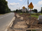 Na zdjęciu widnieje rozkopana ziemia podczas budowy chodnika. Z boku chodnika stoi pomarańczowy znak z wykrzyknikiem w środku