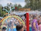 na pierwszym planie sikająca wodą konstrukcja, w tle rozmazane bawiąze się na placu zabaw dzieci