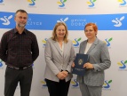 trzy osoby na tle ścianki z logami gminy: kierownik Konrad Skiba, wiceburmistrz Edyta Podmokły oraz wykonawca Iwona Gryglak