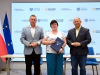 760 tys. zł dla Gminy Dobczyce na budowę magazynu obrony cywilnej od lewej stoi burmistrz Tomasz Suś, obok niego Główna Księgowa renata Banowska, która w trzyma w rękach granatową teczkę typu ofertówka, po prawejs tronie stoi Wojewoda Krzysztof Jan Klęczar, w tle widać flagi Polski i Unii Europejskiej oraz duzy baner z logami Oprogramu Ochrona ludności i obrona cywilna