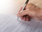 na zdjęciu widać dłoń z długopisem, osoba wypełnia ankietę